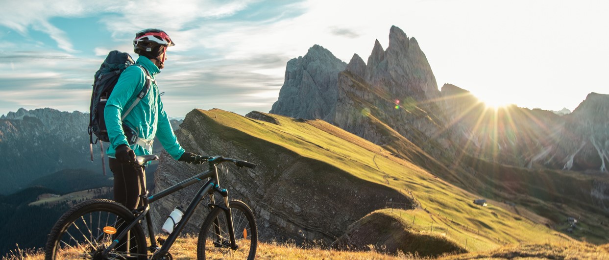 Young man with mountain bike on Seceda mountain peak at sunrise. Puez Odle, Trentino, Dolomites, Italy.